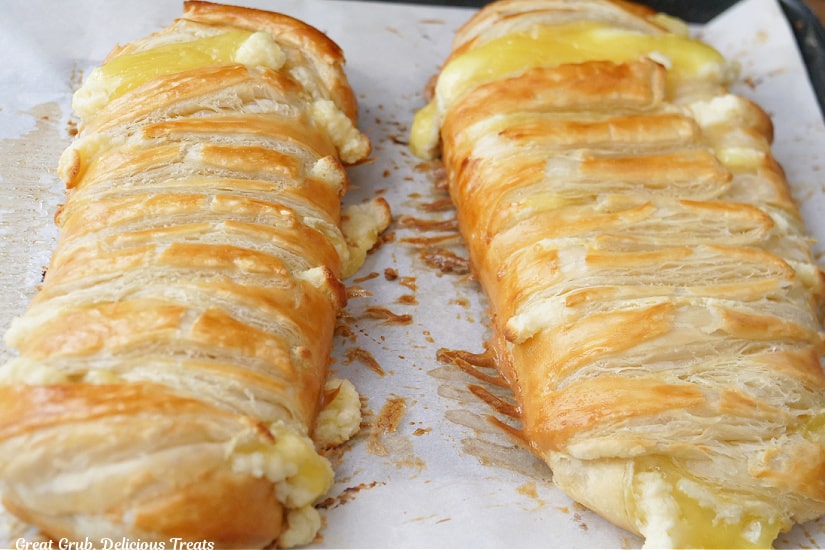 Two whole lemon pastries braids on a baking sheet lined with parchment paper after being pulled out of the oven.