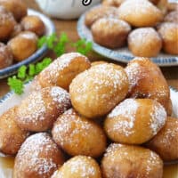 Three white plates with blue trim filled with mini pancake sausage bites with powdered sugar and syrup on them.