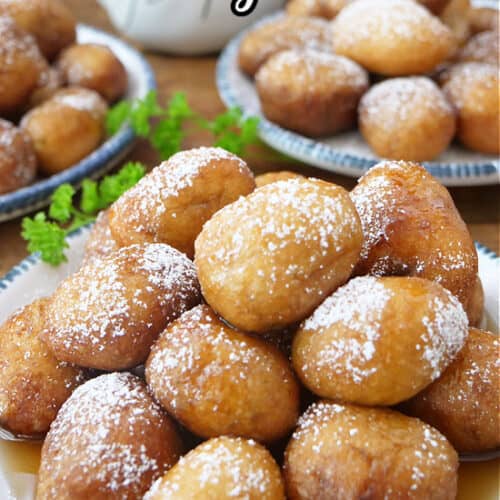 Three white plates with blue trim filled with mini pancake sausage bites with powdered sugar and syrup on them.