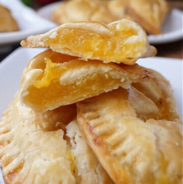 A small stack of nectarine hand pies on a white plate with one cut in half.