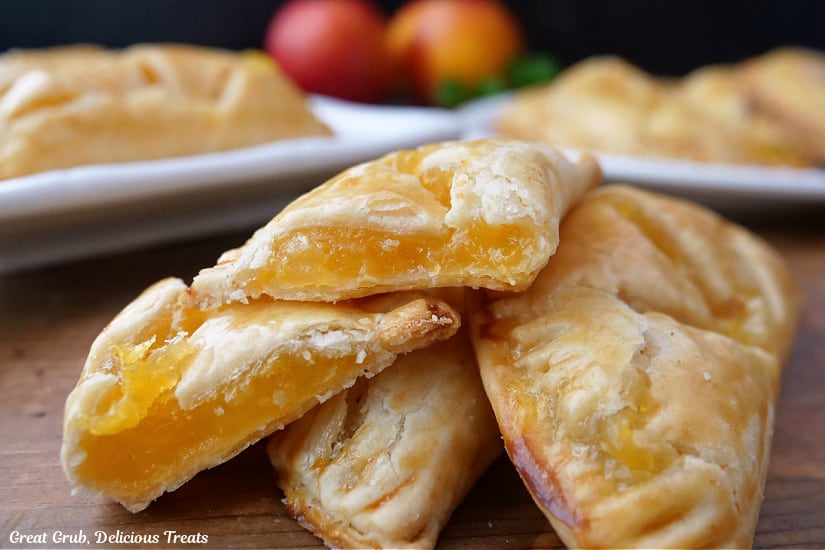 A horizontal photo of nectarine hand pies on a wooden surface with more hand pies on white plates in the background.