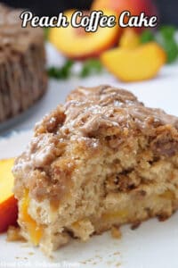 A slice of peach coffee cake on a white plate with peaches in the background.