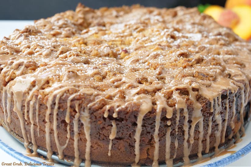 A horizontal photo of a whole peach coffee cake with a brown sugar pecan streusel topping and cinnamon vanilla glaze.