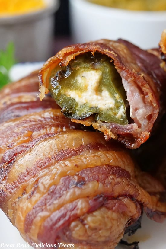 A close up of two jalapeno stuffed peppers wrapped in bacon on a white plate with a bite taken out of it.