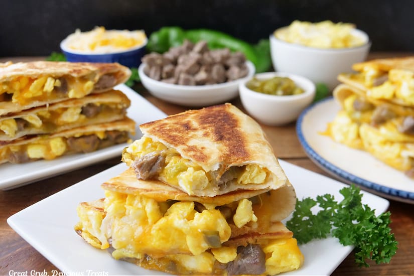 A horizontal photo of white plates with pieces of breakfast quesadillas on them.