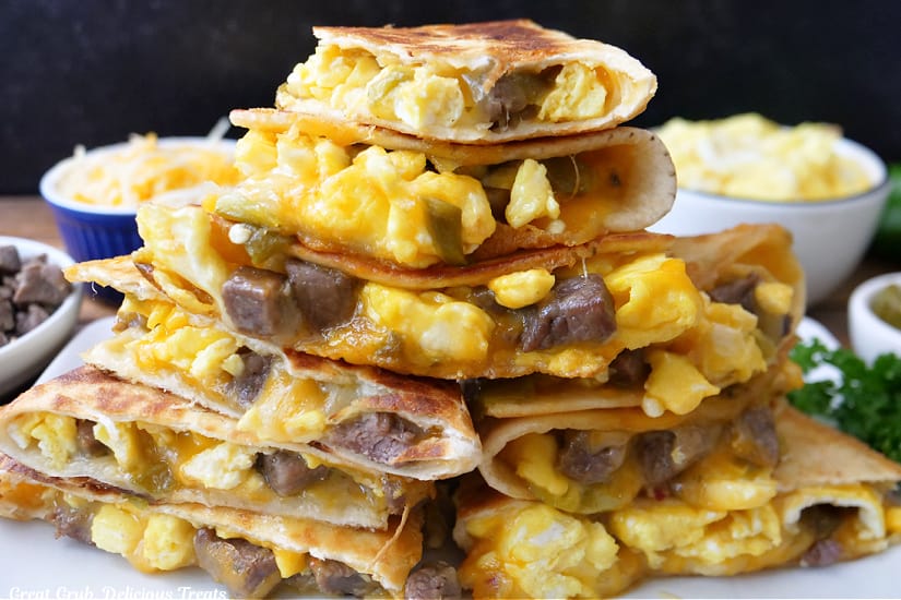 A horizontal photo of a stack of quesadilla wedges filled with eggs, steak, cheese, and green chiles on a white plate.