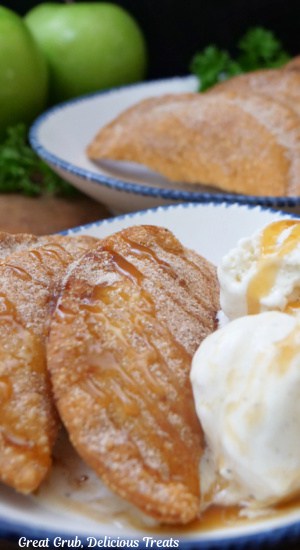 Two white plate with blue trim with fried empanadas on them that are filled with apples and cream cheese.