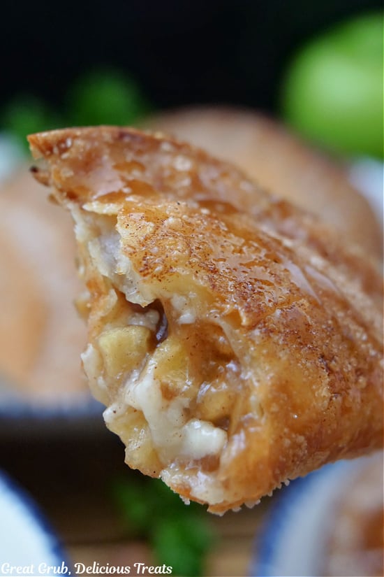 A caramel apple empanada held close to the camera with a bite taken out of it showing the inside ingredients of apples and cream cheese.