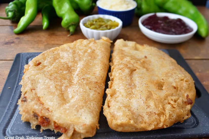 Two crispy cheese quesadillas on a black cutting board after being deep fried.