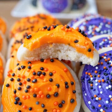 A white plate with mini Halloween cookies with orange and purple frosting and sprinkles on it.