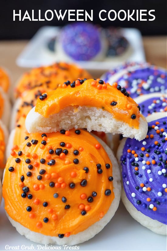 A white plate with mini Halloween cookies with orange and purple frosting and sprinkles on it.