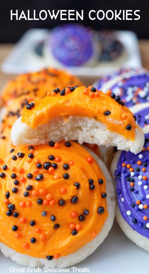 A close up of mini sugar cookies with orange and purple frosting and candy sprinkles on them.