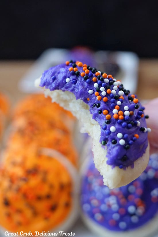 A close up of a bite taken out of a mini Halloween cookie with purple frosting and candy sprinkles on it.