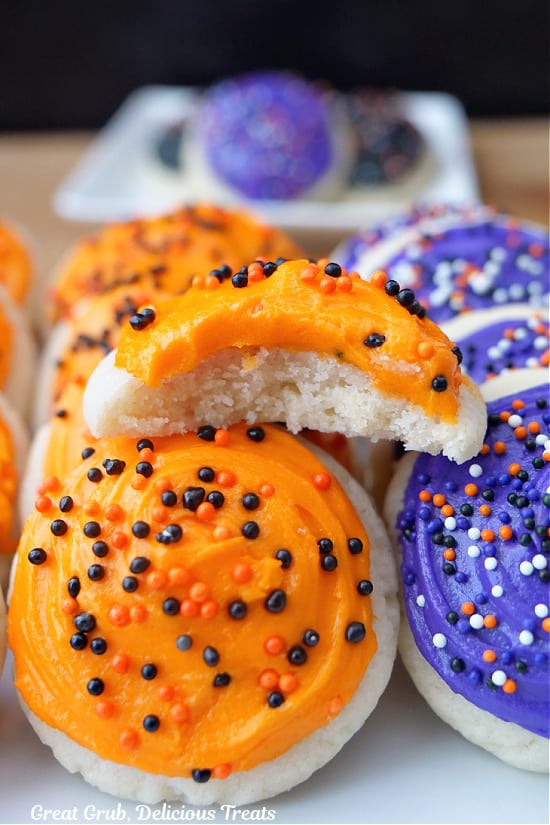 Mini Halloween sugar cookies on a white plate that are frosted with orange and purple buttercream frosting.