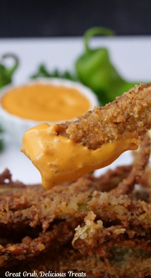 A close up of a hatch green chile fry dipped in an orange spicy sauce.