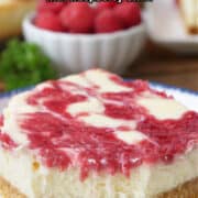 A white plate with blue trim with a serving of lemon cheesecake bar with raspberry swirl on it.