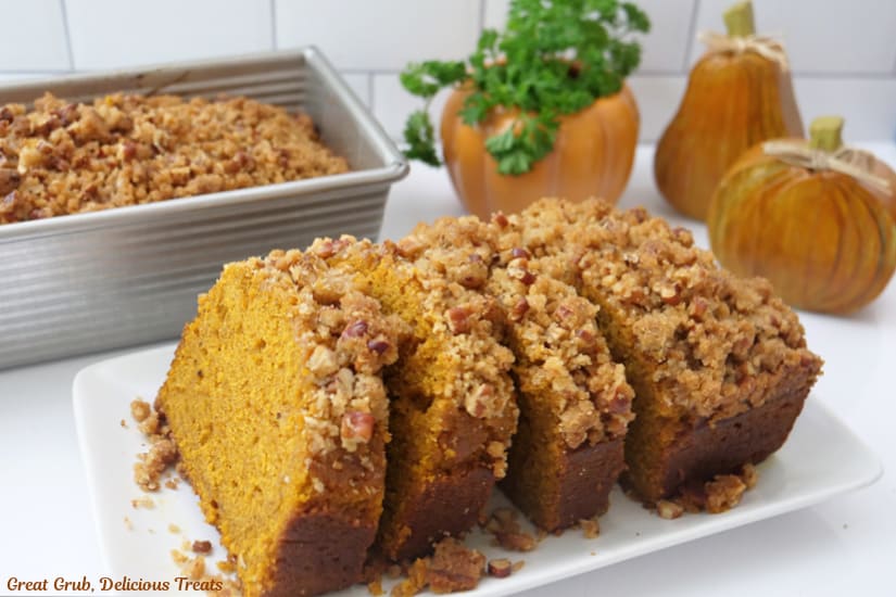 A horizontal photo of slices of pumpkin bread on a white plate with wooden pumpkins with the background.