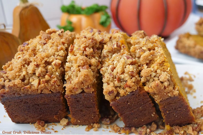 A horizontal photo of slices of pumpkin bread on a white plate with little pumpkins in the background.