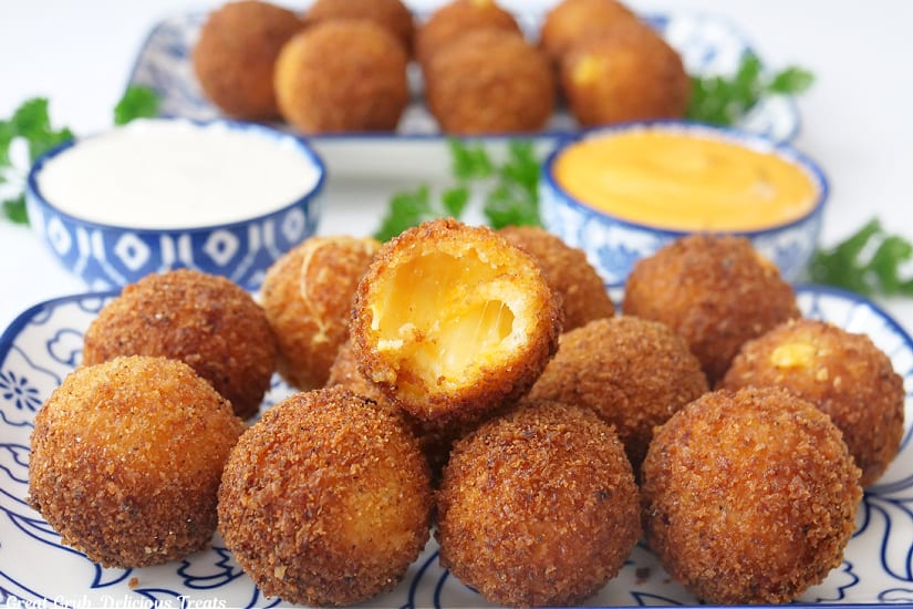 A horizontal photo of two white and blue plates with deep-fried cheese bites on it with two bowls that are filled with dipping sauce.