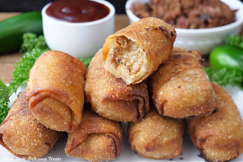 A horizontal photo of 8 fried homemade egg rolls on a white oblong plate.
