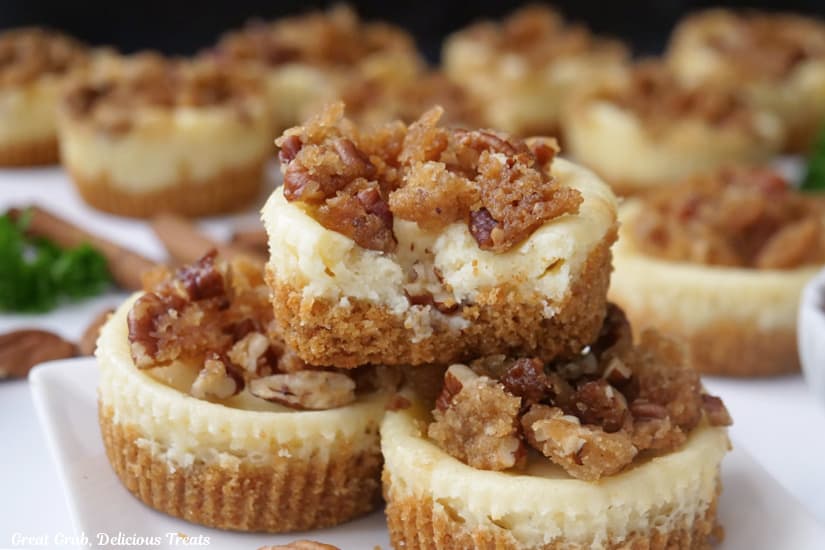 A horizontal photo of about a dozen mini cheesecakes on white plates with a crunchy pecan topping.