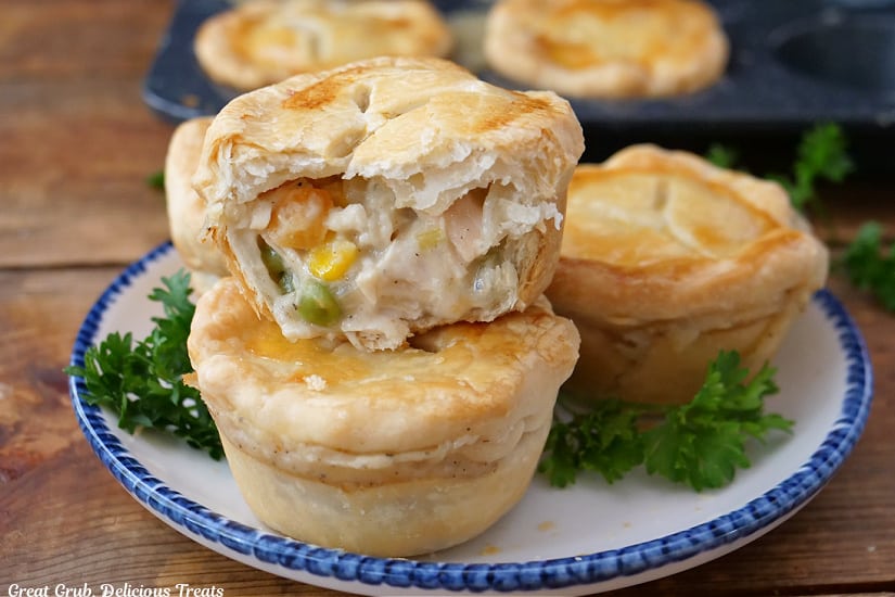 A horizontal photo of a wood surface with a white plate with blue trim with three mini pot pies on it.
