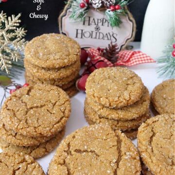 A white surface with seven stacks of molasses cookies, 3 to 4 high, with holiday decorations in the background.