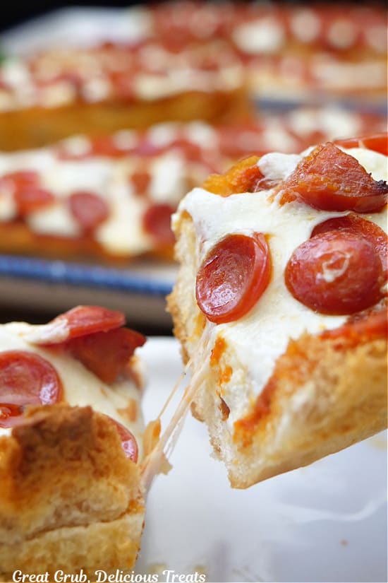 A slice of pepperoni pizza bread cut in half and one half being lifted up showing the melty cheese stretching from one piece to the other.