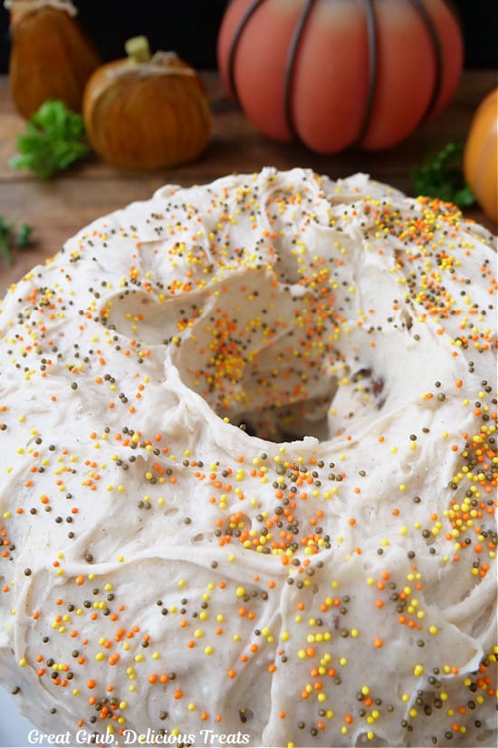 A pumpkin bundt cake with frosting over the whole cake and topped with candied sprinkles.