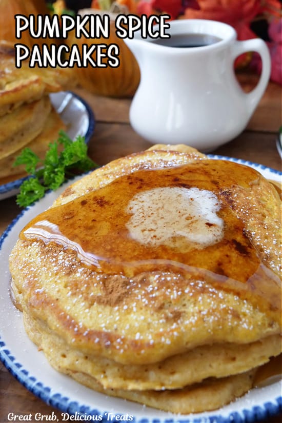 A round white plate with blue trim with three fluffy pumpkin spice pancakes on it, topped with a pad of butter, and syrup.