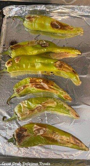 A baking sheet covered with aluminum foil that has six oven roasted green chiles on it.