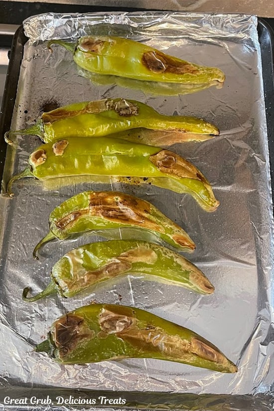Six oven roasted hatch chiles on a baking sheet lined with aluminum foil.