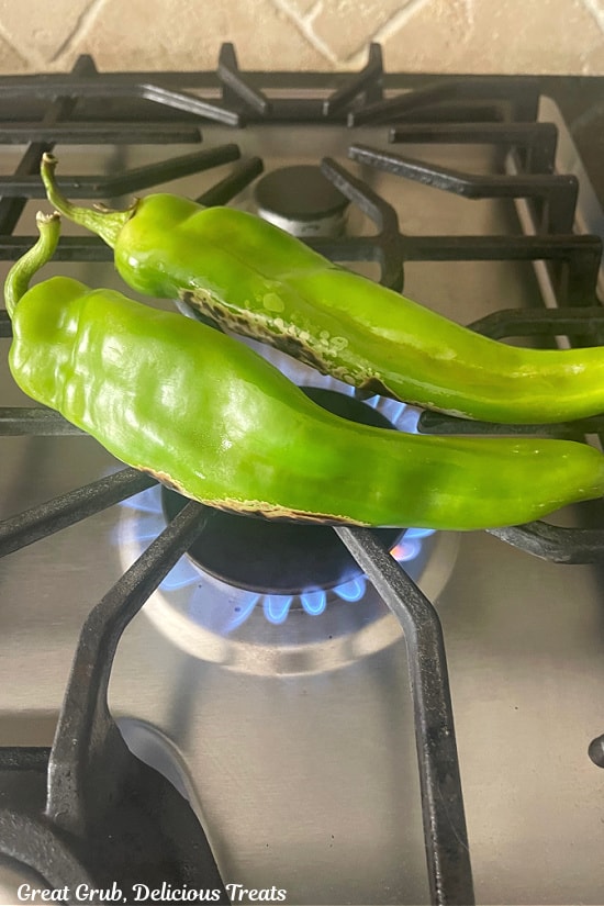Two green chiles being roasted directly on the stove burner with the flame on.
