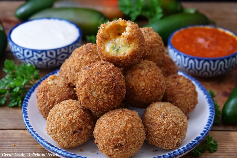 A horizontal photo of crispy cheese balls on a white plate with blue trim with a bite taken out of one of them.