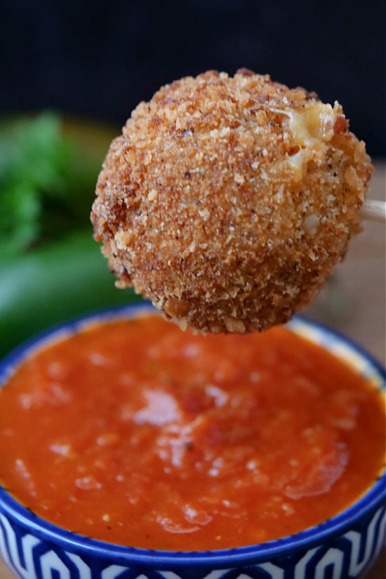 A crispy cheese bite getting ready to be dipped in sauce.