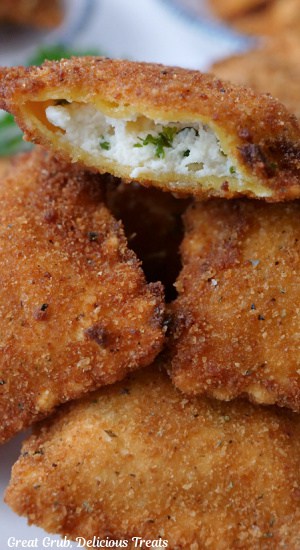A close up of four deep fried raviolis with a bite taken out of one of them.