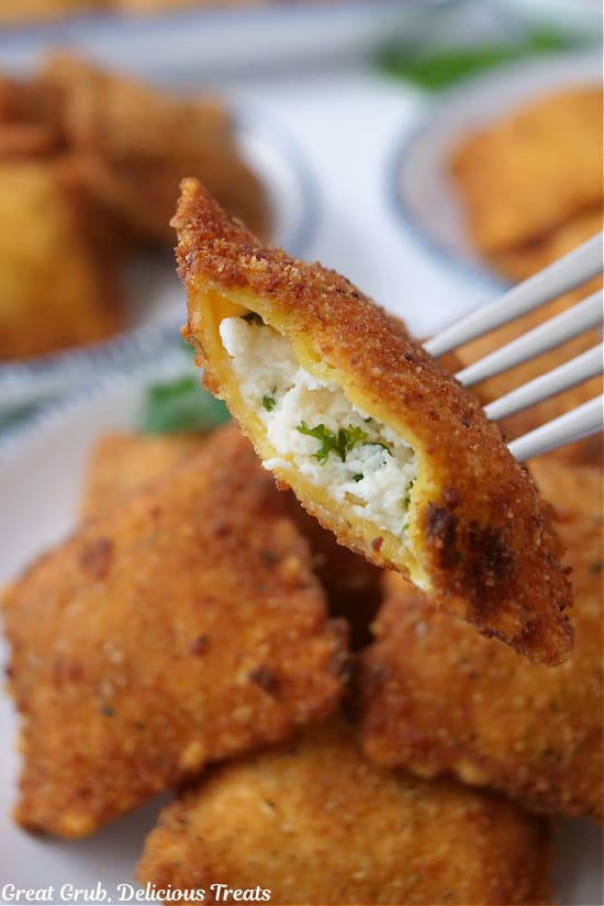 A deep fried ravioli with a bite taken out of it on a fork.