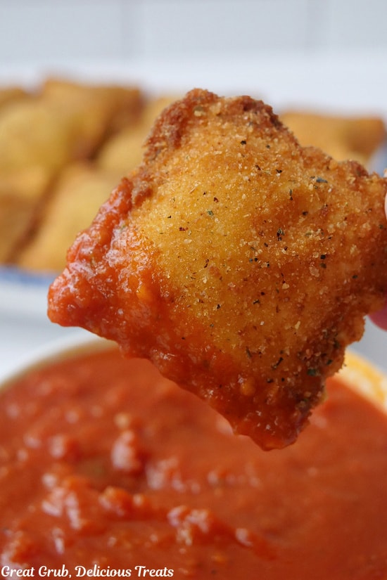 A single toasted ravioli held up after being dipped in marinara sauce.