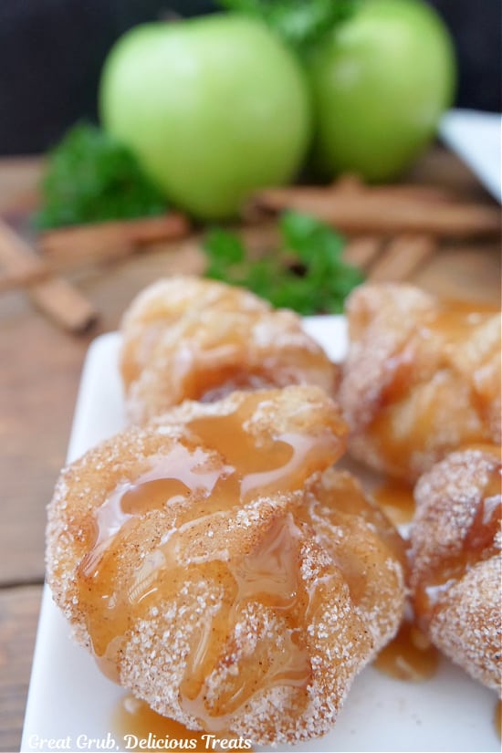 Four apple pie bites on a white plate with caramel sauce drizzled of the top of them.