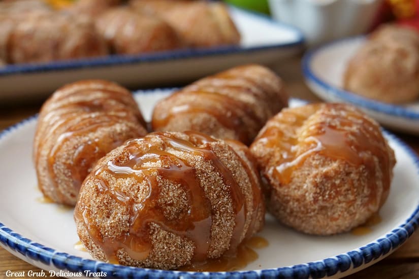 A horizontal photo of four crescents filled with apple pie filling and covered with caramel on a small round white plate with blue trim.