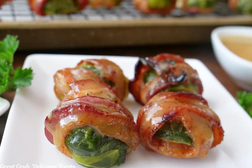 A horizontal photo of a white plate with four brussel sprouts that are wrapped in bacon.