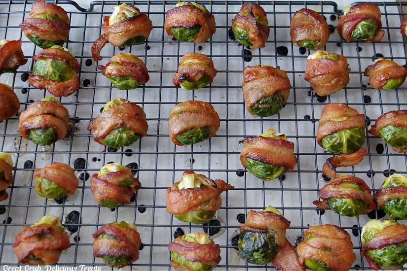 A baking sheet with a wire rack filled with baked bacon wrapped brussel sprout on it.