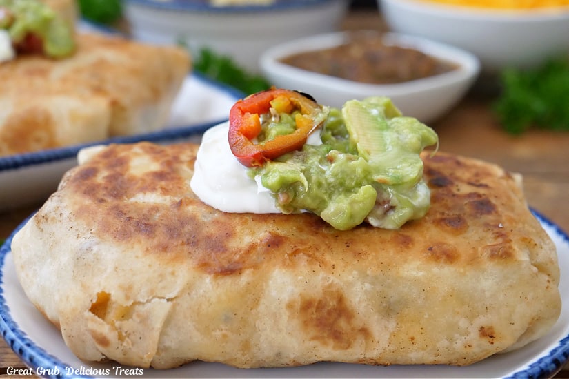 A large grilled breakfast burrito with sour cream and guacamole on top.