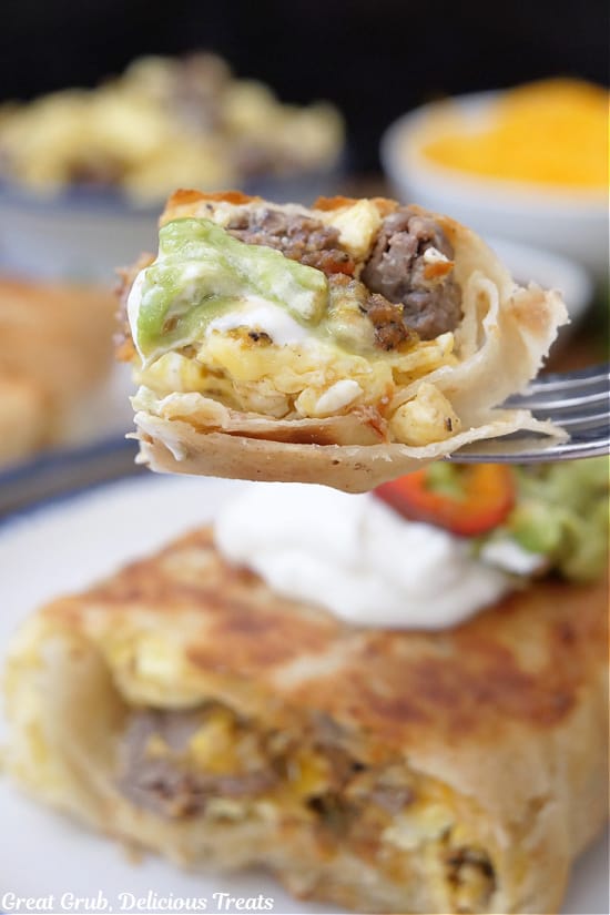 A fork with a bite of steak and egg burrito on it.