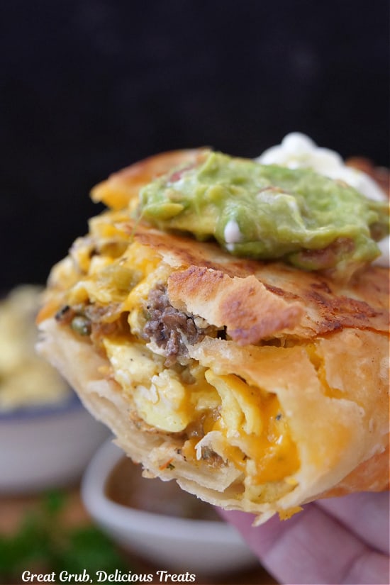 Half of a burrito with steak, egg and cheese, topped with sour cream and guacamole held up close to the camera.