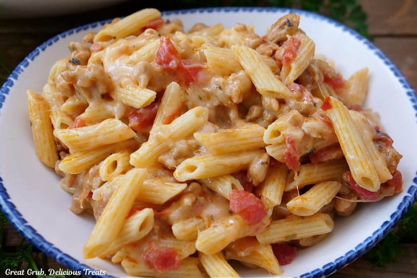 A white serving bowl with blue trim filled with penne pasta and sausage.