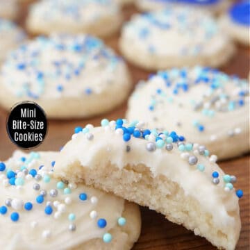 A wood surface with mini Christmas cookies with white frosting and blue frosting and candy sprinkles.