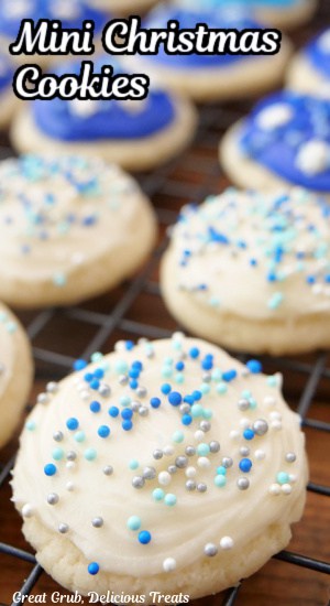 A wire rack with bite-size Christmas sugar cookies on it that are decorated with white and blue frosting and candy sprinkles.