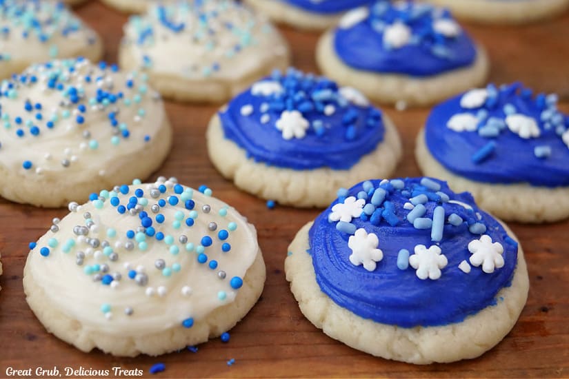 A horizontal photo of bite-size white sugar cookies with white and blue frosting and candy sprinkles on top.