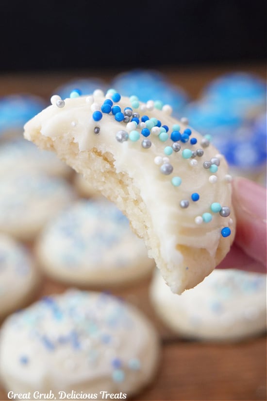 A mini sugar cookie with white frosting and candy sprinkles on top that has a bite taken out of it.